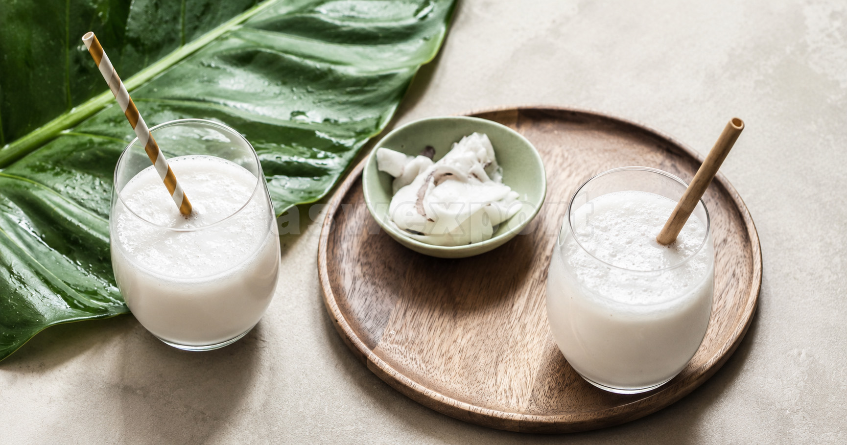 Fresh coconut smoothies served in glass cups with coconut pieces on a wooden tray